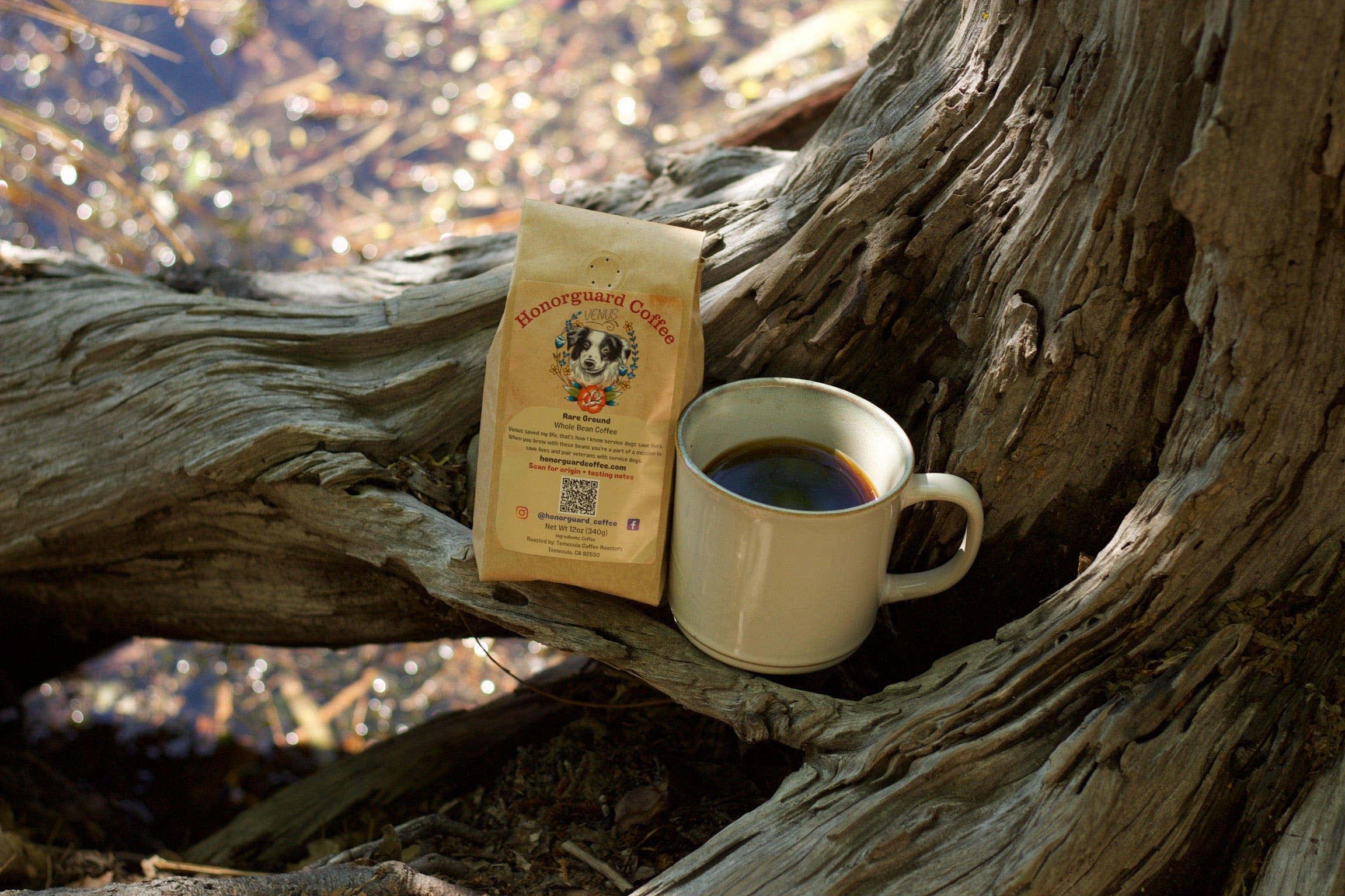 White mug with coffee and a coffee bag on a wooden log by a body of water